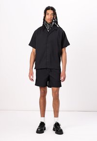 Sort kortærmet skjorte med knapper og matchende shorts i vertikal ribbet tekstur. Sorte sko og hvide sokker fuldender looket.