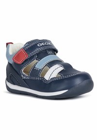 Zapato de cuero marino de tobillo con acentos en blanco y azul claro, cinta de velcro y suela de goma. Presenta detalles de costura y aberturas de ventilación.