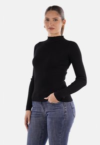 Maglione nero a coste con collo alto e maniche lunghe aderenti, abbinato a jeans in denim blu. Texture liscia e design strutturato.