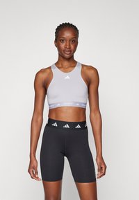 Grå sports-bh med logo, tykke stropper og et lett elastisk bånd; kombinert med sorte høyhalsede shorts med en logo på midjebåndet.