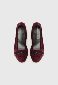 Ballerine in suede bordeaux con texture liscia, dotate di un accento in metallo nero e punta arrotondata. Include dettagli di cucitura sui bordi.