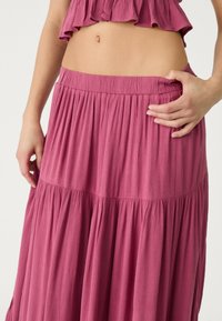 Maxi-Rock aus einem weichen, strukturierten Stoff in Dunkelpink, mit einem gerafften, gestuften Design und einem elastischen Taillenbund.