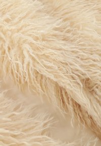 Textured, cream-colored fur with long, tangled strands and a soft, fluffy appearance, showcasing a natural, untrimmed look.