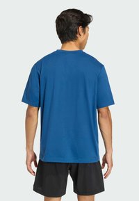 Modré bavlnené tričko s krátkym rukávom, voľný strih, s okrúhlym výstrihom. Bez výrazných vzorov alebo ozdôb. Nosené s čiernymi šortkami.