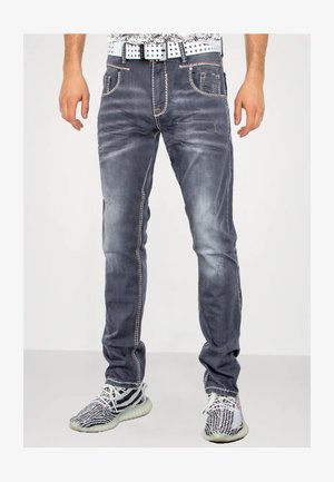 Dunkelgraue Denim-Jeans mit leichter Abnutzung, kontrastierendem orangefarbenem Stitching, Fünf-Taschen-Design und schmaler Passform. Getragen mit gemusterten Sneakers.