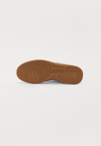 Reebok sportbačių padas, turintis tekstūruotą gumos išorinį padą rudos spalvos su apskrito rašto, logotipo detalizavimas ir šviesiai mėlyna viršutinė medžiaga.