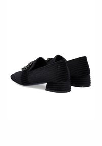 Zapatos de tacón negros con una textura estriada, punta afilada y adornos en la parte delantera. El tacón es corto y de forma cuadrada.