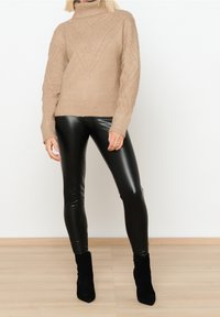 Beige pletený rolák s texturovaným vzorem a žebrovanými manžetami, kombinovaný s černými legínami z umělé kůže a kotníkovými botami.