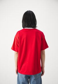 Rode shirt met korte mouwen en een gestructureerde afwerking, voorzien van een witte ronde hals en een losse pasvorm, ontworpen voor casual gebruik.