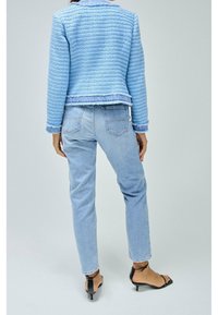 Blå strukturerad kavaj med fransade kanter, kombinerad med ljusblå jeans och svarta remsandaler med klack. Fokusera på lager av tyg och avslappnad passform.