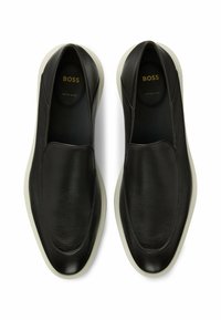 Bottines en cuir noir à enfiler avec une surface texturée, un design élégant et une semelle en caoutchouc blanc. Marquage doré visible à l'intérieur.