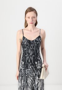 Zwart-witte gestreepte mouwloze jurk met een V-hals, slanke bandjes en een vloeiende silhouet; vergezeld van een beige clutch.