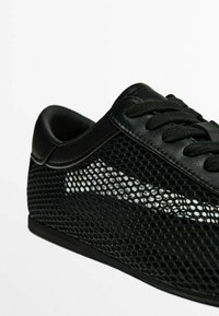 Mustat lenkkarit, joissa on verkkokangasta sivuilla, mustat nauhat sekä nahkareunukset nilkan ja nauhojen ympärillä, esitetty valkoista taustaa vasten.