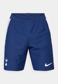 Blå sportsbukser med vertikal ribbet tekstur, elastisk talje og hvidt Nike-logo på højre ben. Har sidelommer i net.