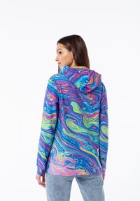Sudadera con capucha colorida que presenta un patrón de mármol en espiral en azul, rosa, verde y amarillo. Tejido suave con un corte relajado y mangas largas.
