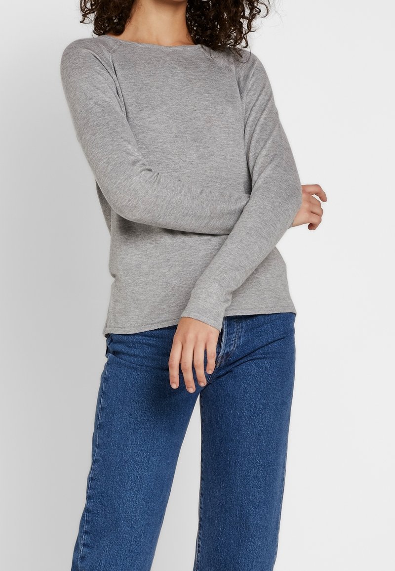 Grauer Langarmpullover mit Rundhalsausschnitt, aus weichem Material gefertigt. Kombiniert mit blauen Denim-Jeans, die eine lässige Passform zeigen.