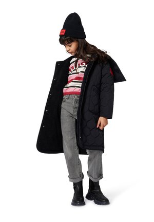 Manteau matelassé noir avec une doublure intérieure douce, porté sur une chemise rayée rouge, rose et blanche, associé à un jean gris et des bottines noires.