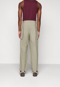 Cargo kalhoty ve světlé olivové barvě, vyrobené z měkkého materiálu. Mezi jejich vlastnosti patří široké nohavice, několik bočních kapes a pohodlný střih.