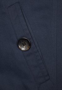 Tela azul marino con tejido texturizado, con un bot ón negro prominente. Se observa un bolsillo vertical en el lado izquierdo.