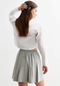 Chemise blanche à manches longues, associée à une mini-jupe plissée gris clair avec une taille élastique et des rayures verticales.