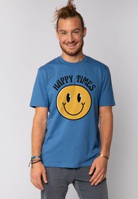 Blauwe katoenen T-shirt met korte mouwen, voorzien van een grote gele glimlachende gezichtgrafiek en de tekst "HAPPY TIMES" in het zwart erboven.
