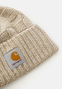 Cappello a maglia beige con una trama a coste, caratterizzato da una toppa grigia con un logo arancione. Materiale morbido in misto lana.