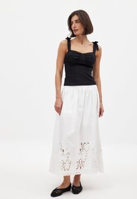Top aderente nero con dettaglio arricciato sul busto e spalline spesse, abbinato a una gonna maxi bianca con complessi merletti sul orlo. Ballerine nere.