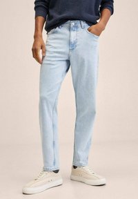 Vaqueros de mezclilla azul claro con corte recto, diseño de cinco bolsillos y bragueta de botones. Combinados con zapatillas de color crema.