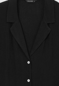 Camicia nera con bottoni, in un tessuto testurizzato, con colletto a punta e bottoni bianchi, caratterizzata da una vestibilità rilassata e da un design minimalista.