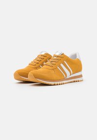 Zapatillas deportivas de ante amarillo con detalles en cuero blanco, puntera perforada y cuello acolchado. Presentan rayas blancas y una suela texturizada.