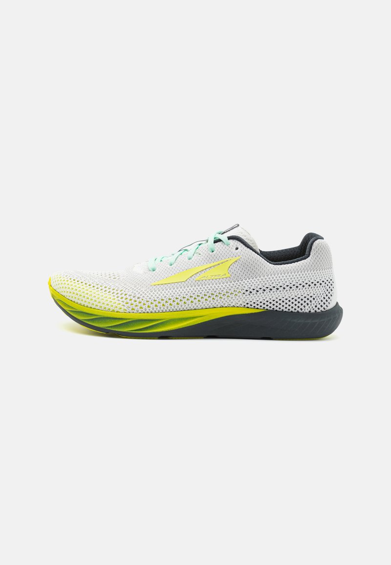 Chaussure de course légère en maille blanche avec des accents verts et jaunes. Caractéristiques d'une semelle rembourrée et d'un design de talon prononcé pour la stabilité.