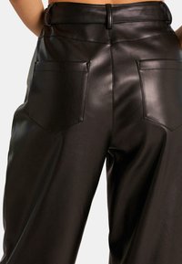 Zwarte neplederen broeken met een hoge taille, wijde pijpen en twee achterzakken. Kenmerkt zich door een gladde textuur en subtiele stikdetails.