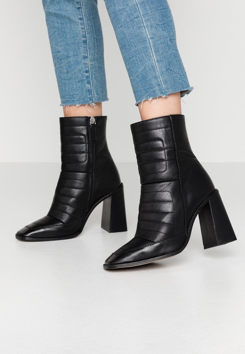 Bottines en cuir noir avec texture matelassée, bout pointu et talon épais. Comprend une fermeture éclair latérale.