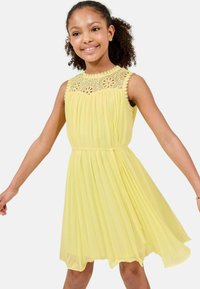 Abito giallo plissettato con yoke in pizzo floreale, design senza maniche e cintura in vita. Il tessuto morbido e leggero crea una silhouette fluente.