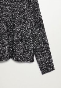 Manche en tissu tricoté texturé noir et blanc d'un pull à manches longues présenté sur un fond blanc uni.