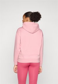 Hettegenser i lys rosa med en avslappet passform, ribbestrikkede mansjetter og nederkant. Båret med matchende rosa leggings, sett fra baksiden.
