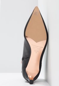 Chaussure noire à bout pointu et talon, posée sur le talon, montrant la semelle beige avec la marque Ted Baker et la taille 37.