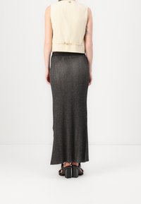 Un gilet beige court avec une coupe droite, associé à une longue jupe côtelée gris foncé. Des sandales noires à talons épais complètent l'ensemble.