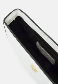 Biała torba z czarnymi wykończeniami i złotą klamrą. Wnętrze wykonane z czarnej tkaniny. Prosty design z gładką powierzchnią i czystymi liniami.