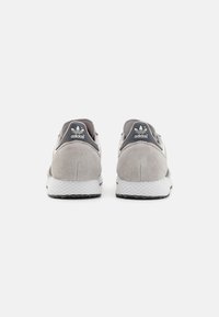 Pair of gray suede Adidas sneakers viewed from the back, featuring white textured midsoles and black heel tabs with Adidas logo.