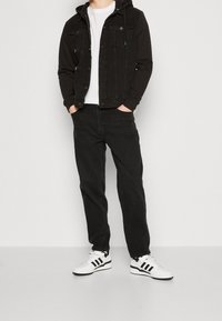 Svart denimjacka med huva, vit t-shirt, svarta jeans och vita sneakers med svarta ränder. Avslappnad outfit med en lös passform.