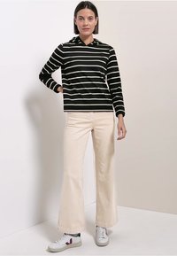 Czarna i biała prążkowana bluza z długim rękawem i kapturem, zestawiona z jasnymi, szerokimi spodniami i białymi trampkami z czerwonymi akcentami.