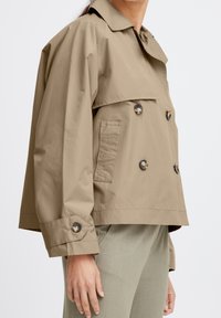 Giacca cropped beige chiaro realizzata in tessuto liscio, con colletto classico, bottoni doppi e tasca laterale.