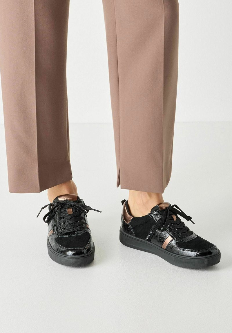 Baskets noires présentant un mélange de matières en cuir verni brillant et en daim mat, avec un accent métallique et des lacets ronds.