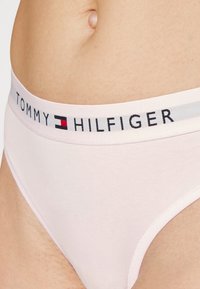 Svetloružové bavlnené nohavičky s širokým elastickým pásom, na ktorých je v čiernej a červenej farbe branding "TOMMY HILFIGER" s šedým akcentovým pruhom.