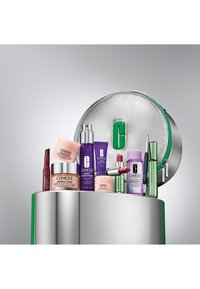 Set de cuidado de la piel de Clinique en una bolsa redonda plateada con acentos verdes. Incluye cremas y sueros en envases rosa, púrpura y verde.