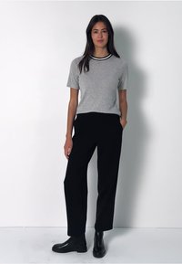 Harmaa puuvillapaita, jossa on mustavalkoinen ribbineck, yhdistetty korkeavyötäröisiin mustiin housuihin ja mustiin nilkkureihin. Yksinkertainen, rento istuvuus.