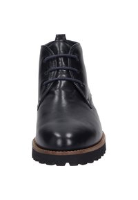Bottines chukka en cuir noir avec bout rond, dotées de six œillets pour les lacets, d'une semelle texturée et d'un bord marron contrastant autour de la base.