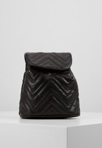 Schwarzer Leder-Rucksack mit Zickzack-quiltetem Muster, umschlagbarem Deckel und abgerundetem Boden. Hat eine weiche Textur und ein minimalistisches Design.
