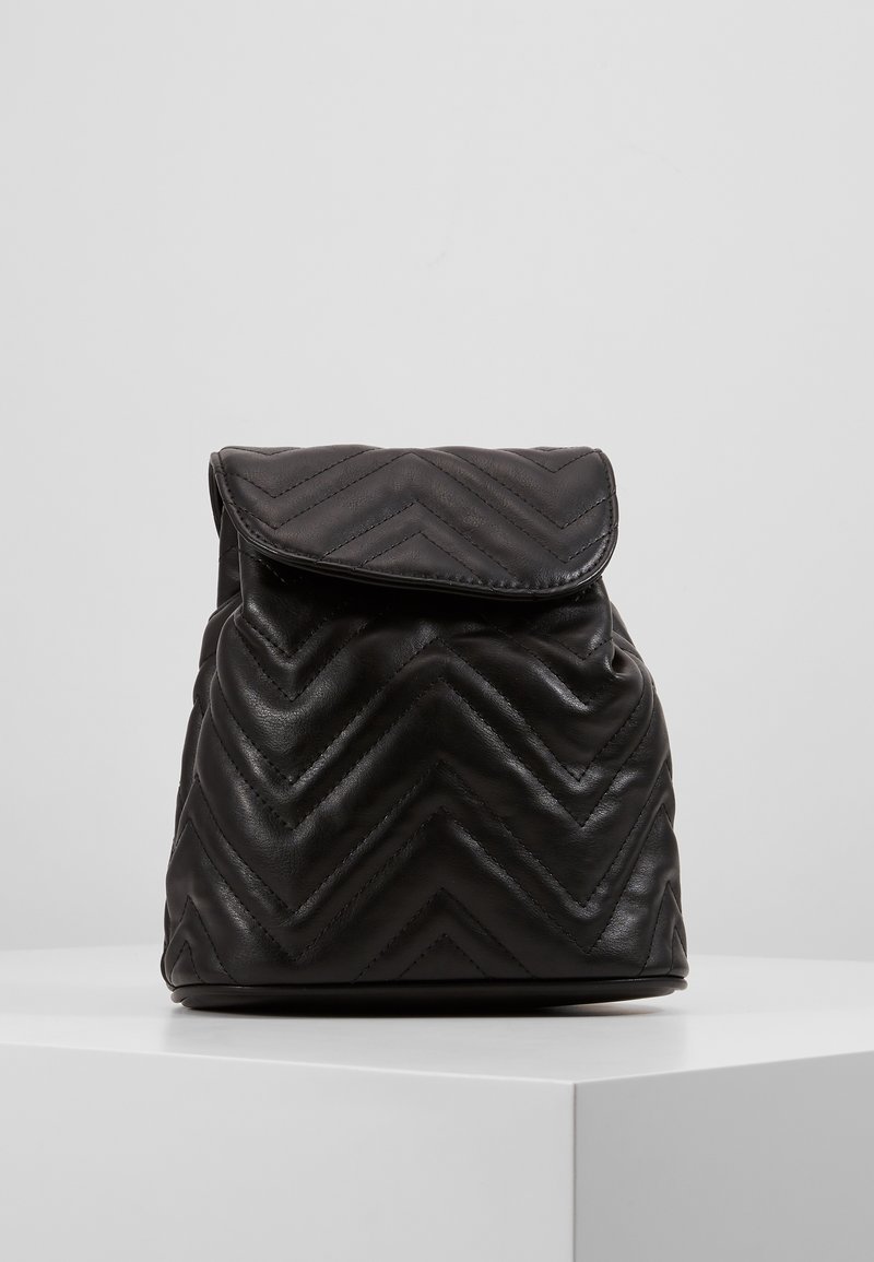 Schwarzer Leder-Rucksack mit Zickzack-quiltetem Muster, umschlagbarem Deckel und abgerundetem Boden. Hat eine weiche Textur und ein minimalistisches Design.